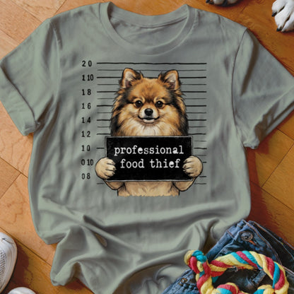 Pomeranian dog mugshot with "professional food thief" sign on a light grey t-shirt.