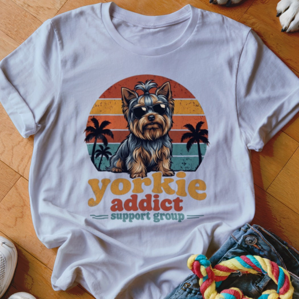 A white t-shirt featuring a retro graphic of a Yorkshire terrier wearing sunglasses with palm trees and sunset stripes.