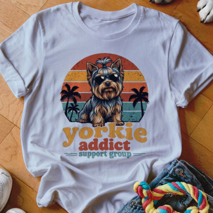 A white t-shirt featuring a retro graphic of a Yorkshire terrier wearing sunglasses with palm trees and sunset stripes.