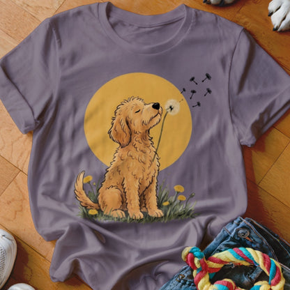 A gray t-shirt featuring an illustration of a golden doodle blowing dandelion seeds against a yellow sun.