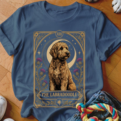 A dark blue t-shirt featuring a tarot card graphic of a Labradoodle surrounded by thistles and a crescent moon.