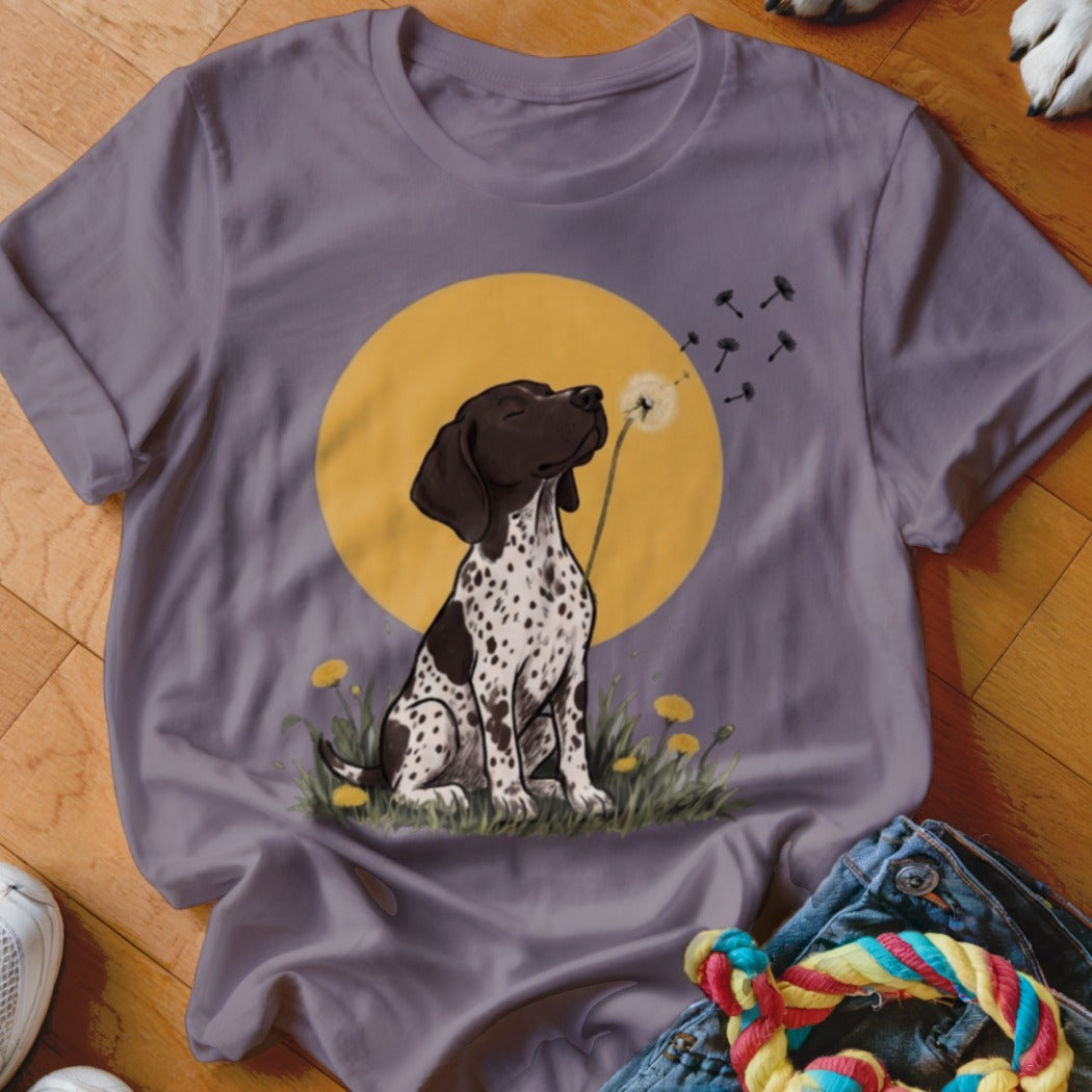 A grey t-shirt featuring a graphic of a spotted puppy blowing dandelion seeds against a yellow circle.