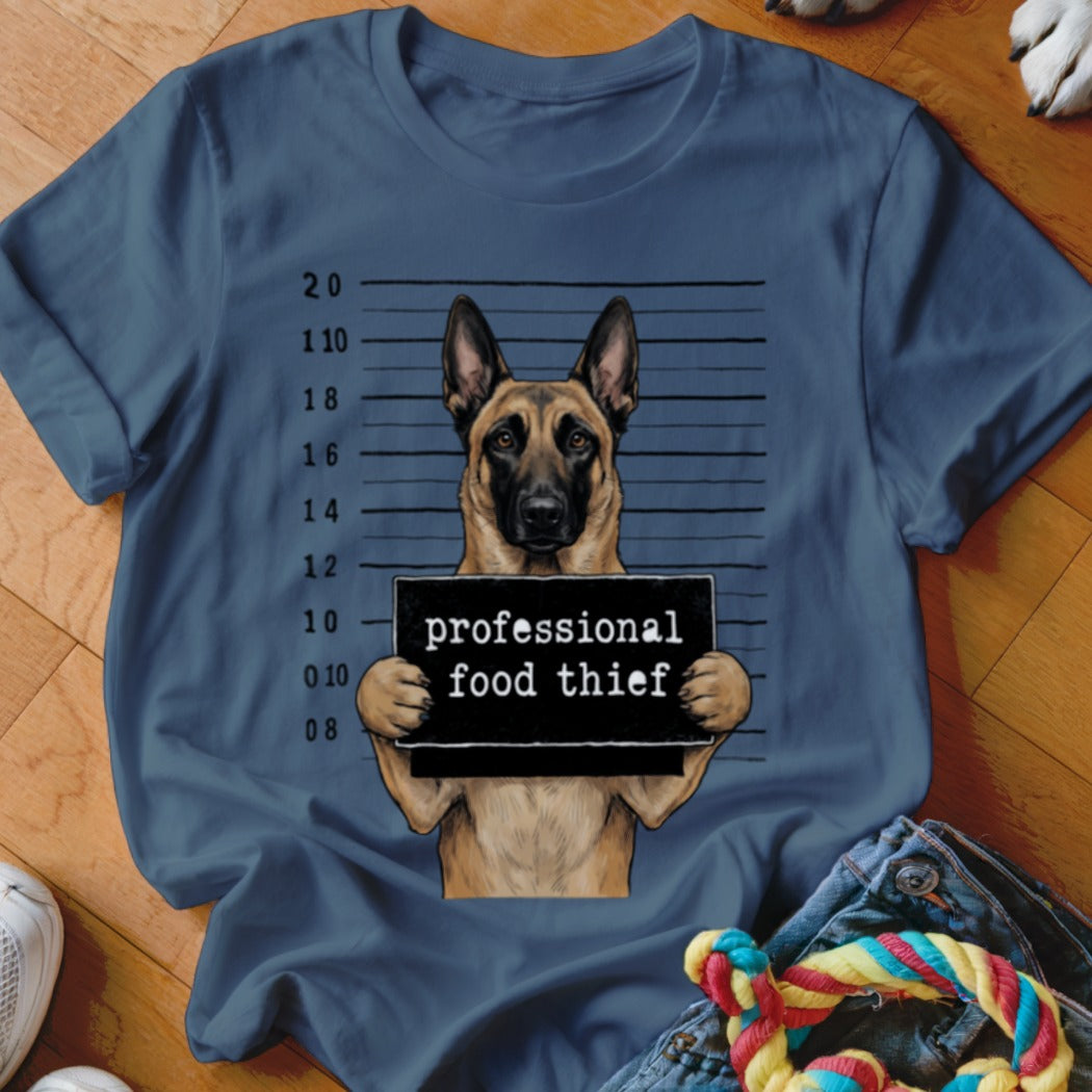 German Shepherd mugshot with "professional food thief" sign on blue t-shirt.