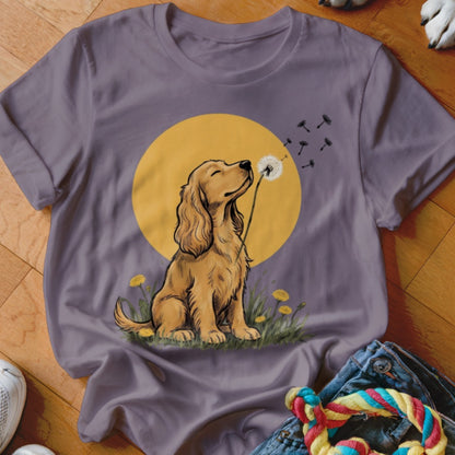 A grey crewneck t-shirt featuring a graphic of a golden spaniel blowing a dandelion.