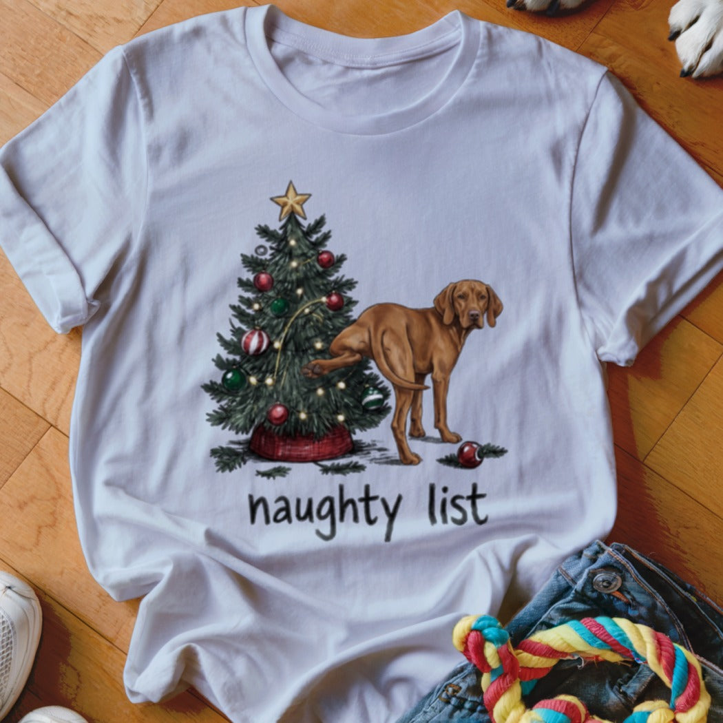 A white crewneck t-shirt features a graphic of a dog lifting its leg on a Christmas tree, with the text "naughty list" below.