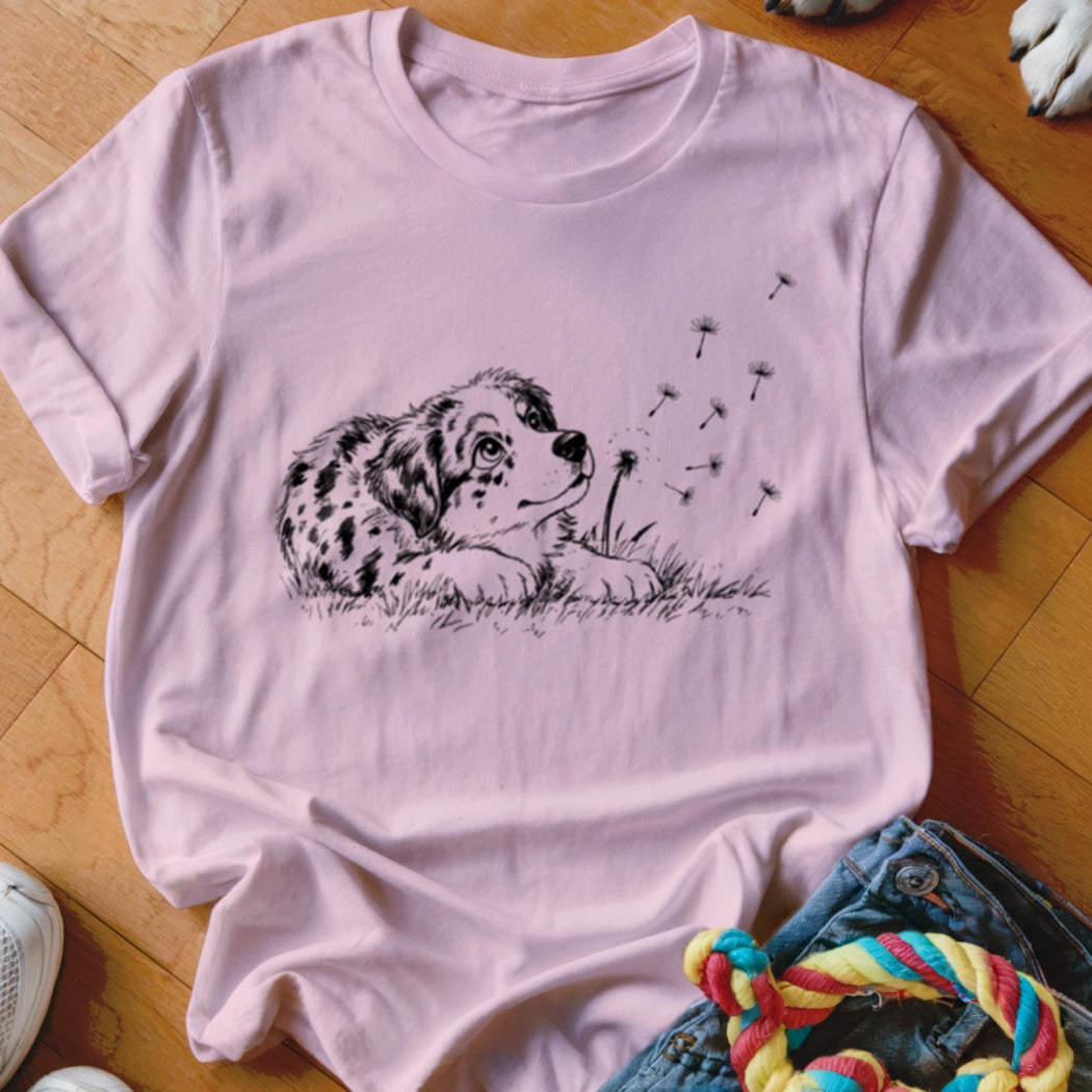 Light pink crewneck t-shirt featuring a black line art graphic of a spotted puppy watching dandelion seeds blow away.