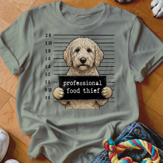 Goldendoodle in mugshot holding "professional food thief" sign on a light green t-shirt.