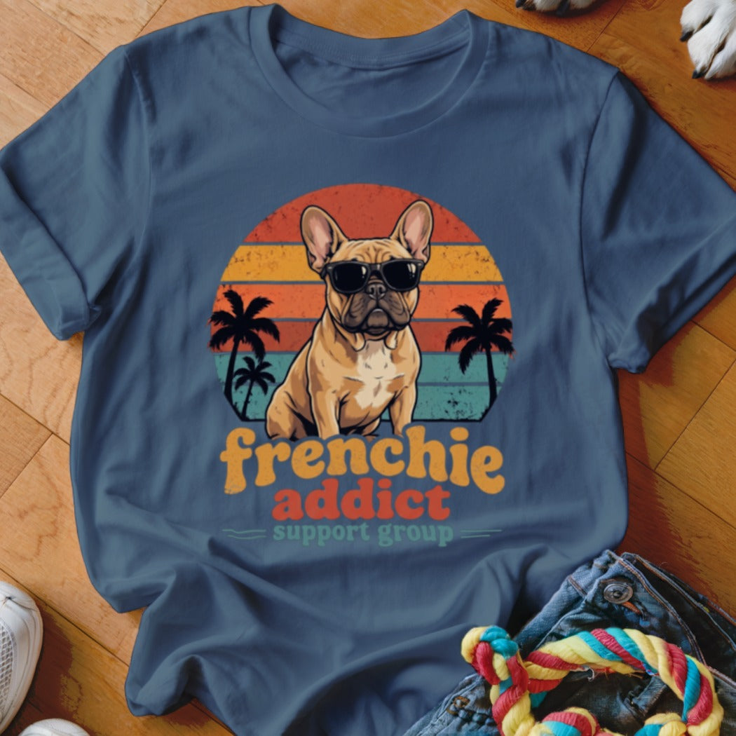 A blue t-shirt featuring a retro graphic of a French bulldog wearing sunglasses before a sunset.