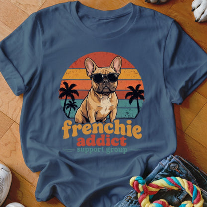 A blue t-shirt featuring a retro graphic of a French bulldog wearing sunglasses before a sunset.