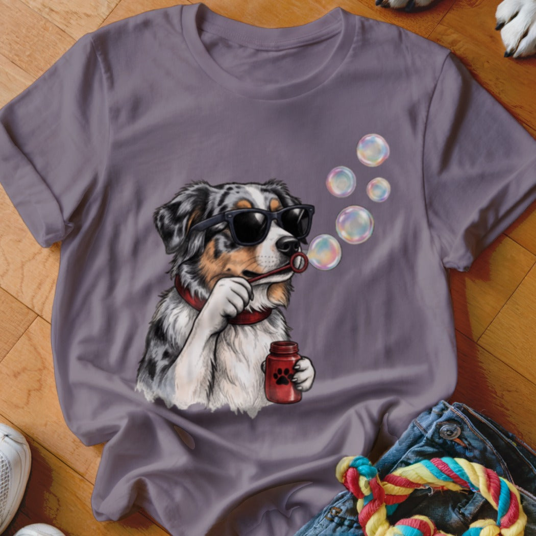 A purple t-shirt featuring a graphic of an Australian Shepherd wearing sunglasses and blowing bubbles.