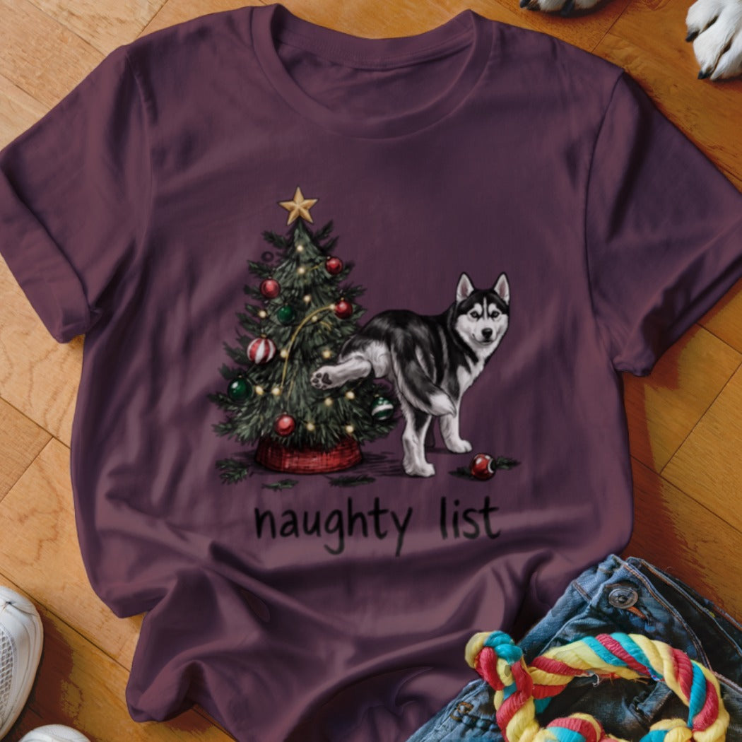 A maroon t-shirt featuring an illustration of a husky urinating on a Christmas tree with the text "naughty list".