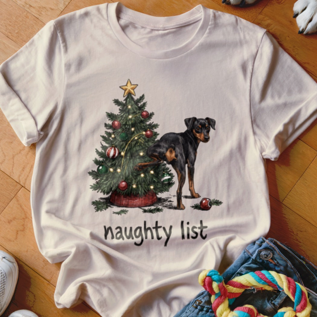 Dog marking a Christmas tree with "naughty list" text on a t-shirt.