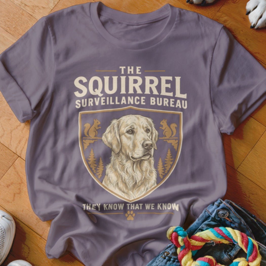 A purple t-shirt featuring a Golden Retriever illustration and text reading The Squirrel Surveillance Bureau.