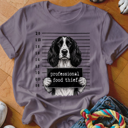 English Springer Spaniel in mugshot holding "professional food thief" sign on grey t-shirt.