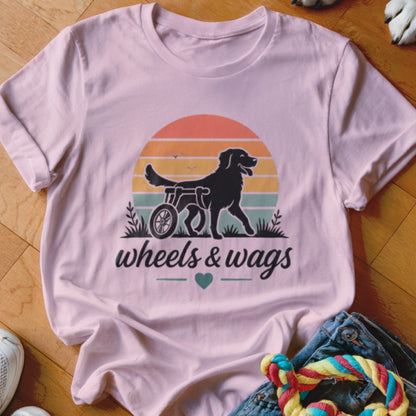 Pink t-shirt with graphic of dog in wheelchair, sunset, and text "wheels & wags".