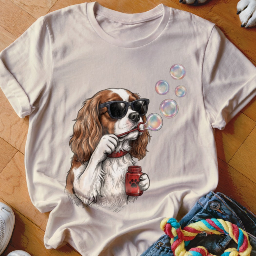 A light-colored t-shirt features a graphic of a Cavalier King Charles Spaniel wearing sunglasses and blowing soap bubbles.