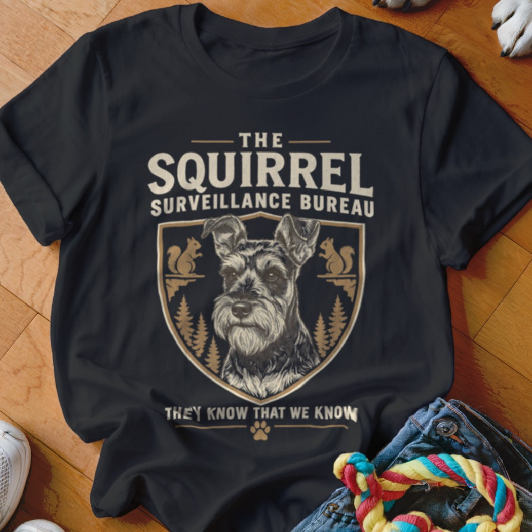 A black t-shirt features a graphic with a Schnauzer, squirrels, pine trees, and text reading The Squirrel Surveillance Bureau.