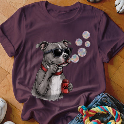 A dark purple t-shirt features a graphic of a grey dog wearing sunglasses and blowing soap bubbles.