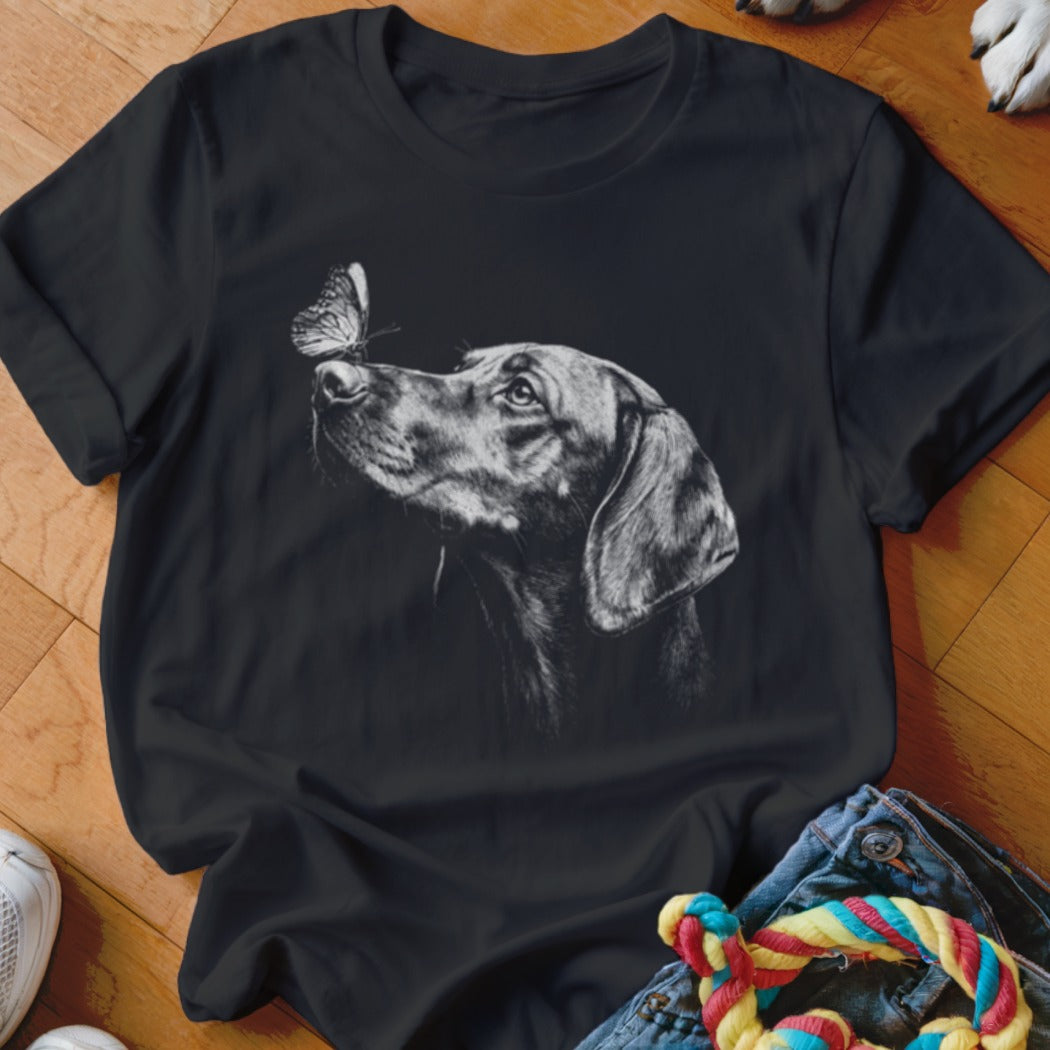 A black t-shirt features a white graphic of a dog looking at a butterfly on its nose.