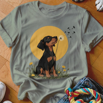 Sage green t-shirt featuring a graphic of a puppy blowing dandelion seeds against a yellow circle background.