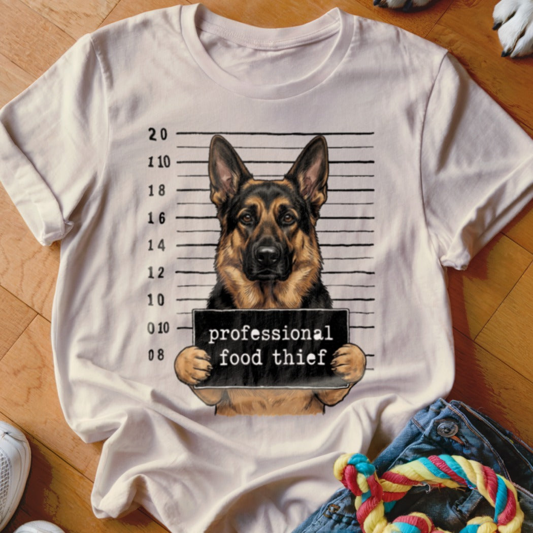 German Shepherd mugshot with "professional food thief" sign on a t-shirt.