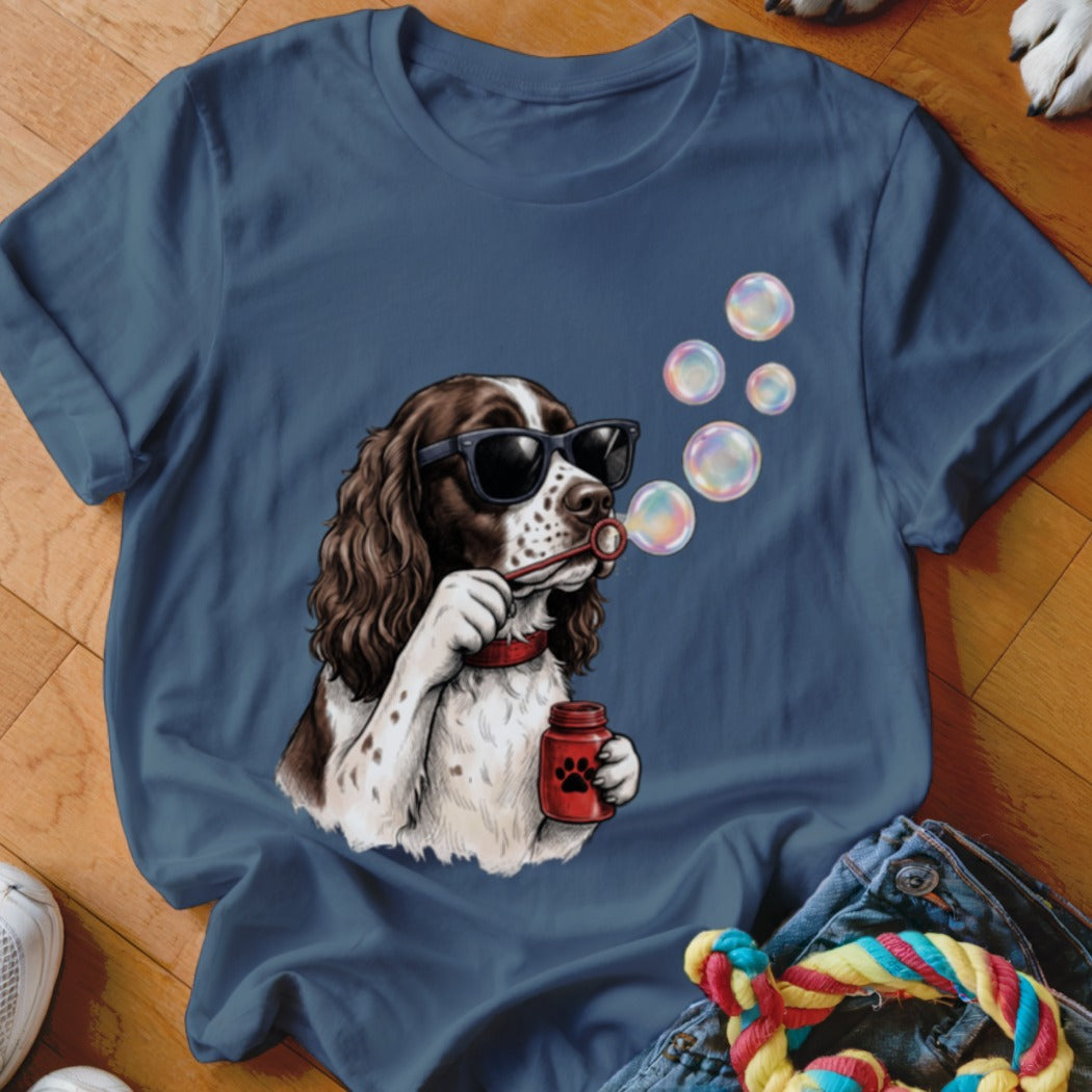 A blue t-shirt featuring an illustration of a brown and white dog wearing sunglasses and blowing bubbles.