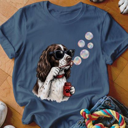 A blue t-shirt featuring an illustration of a brown and white dog wearing sunglasses and blowing bubbles.
