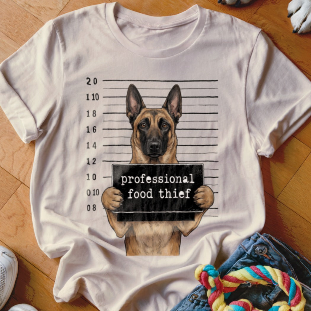 German Shepherd mugshot with "professional food thief" sign on a white t-shirt.