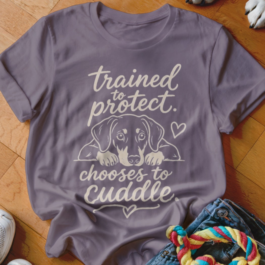 Purple t-shirt with a dog illustration and text "trained to protect, chooses to cuddle".
