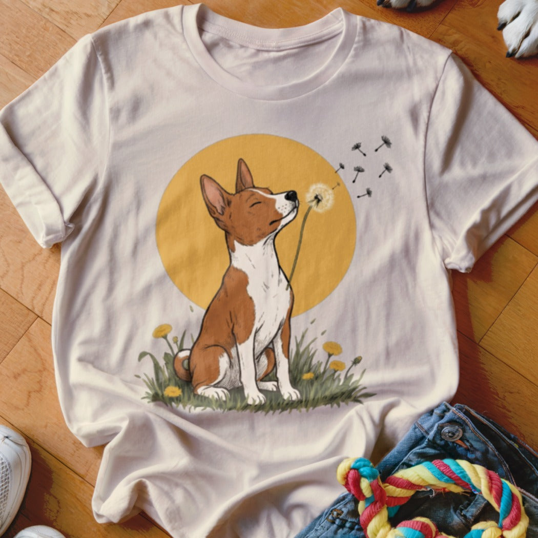 A light beige t-shirt featuring an illustration of a brown and white dog blowing dandelion seeds.