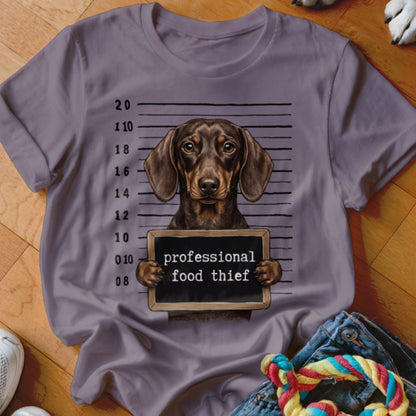 Dachshund holding a sign that reads "professional food thief" in a mugshot.
