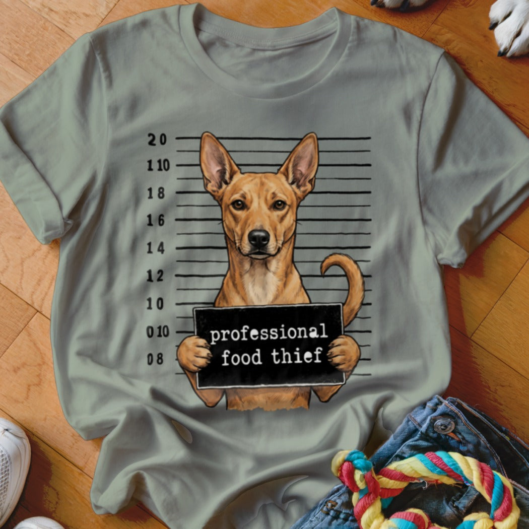 Dog mugshot with sign reading "professional food thief" on grey t-shirt.