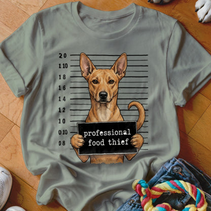 Dog mugshot with sign reading "professional food thief" on grey t-shirt.
