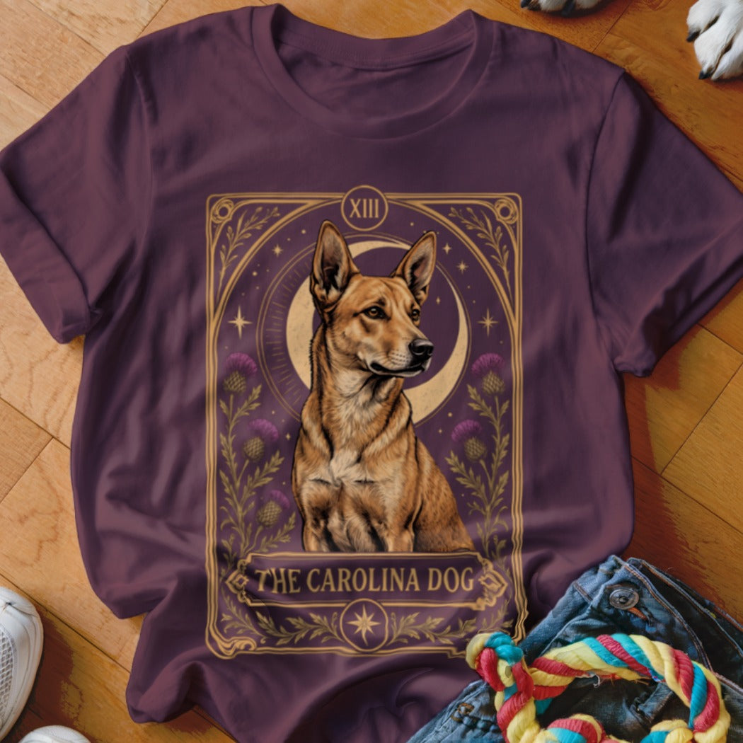 A maroon t-shirt displays a tarot-style graphic of a Carolina Dog surrounded by crescent moons and flowers.