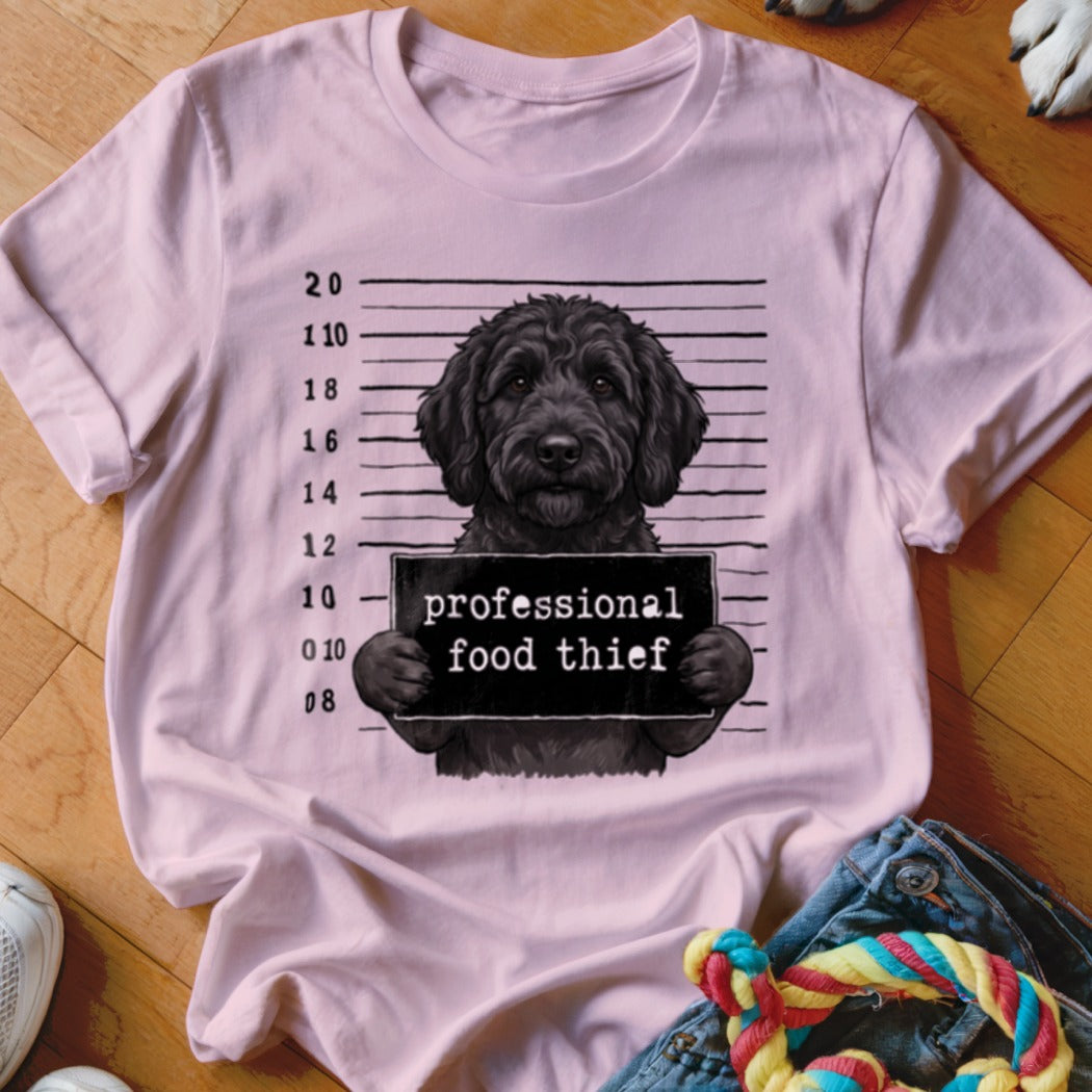 Black doodle dog mugshot with "professional food thief" sign.
