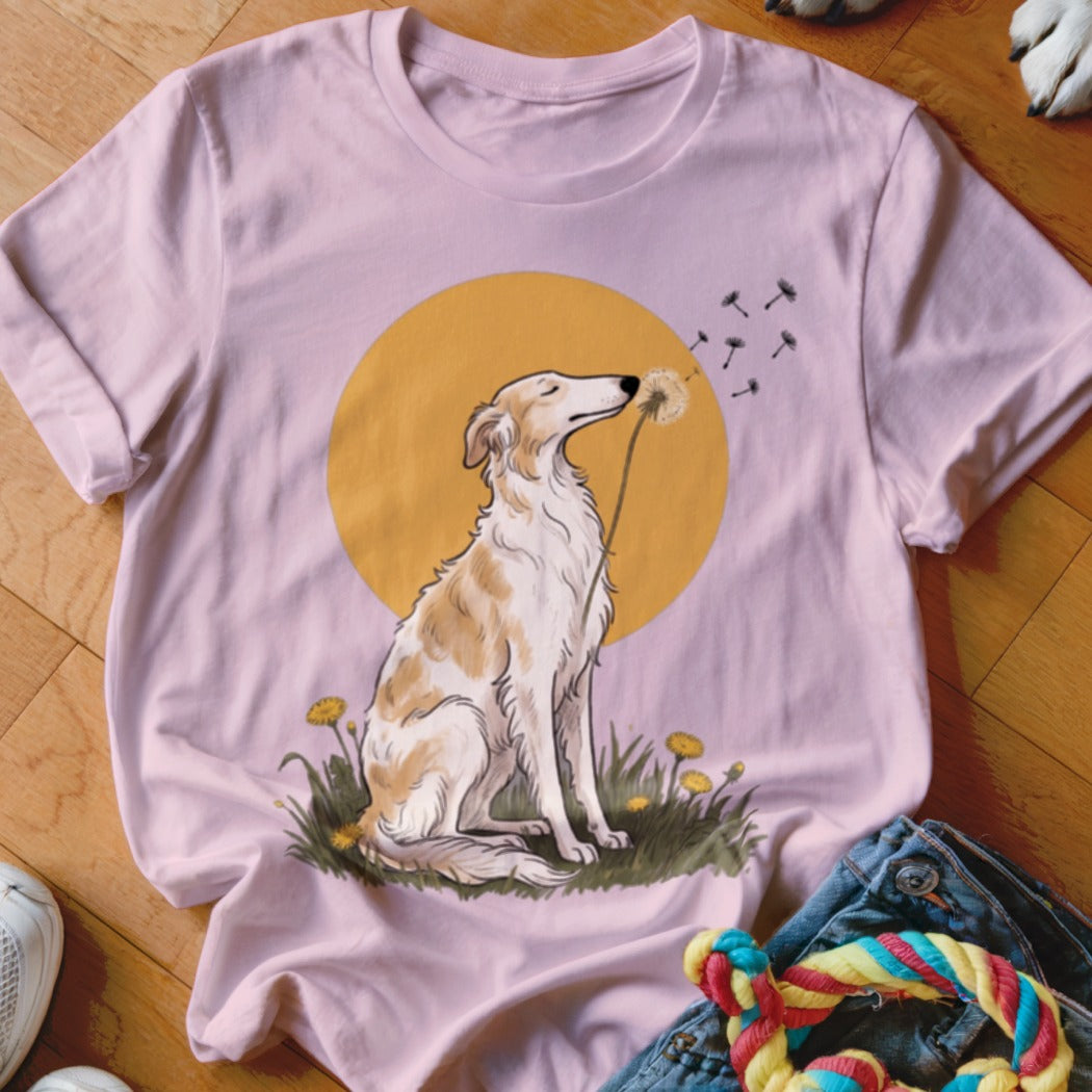 Light pink t-shirt featuring an illustration of a dog sitting in grass and blowing dandelion seeds.