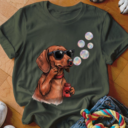An olive green t-shirt featuring a graphic of a dachshund wearing sunglasses and blowing bubbles.