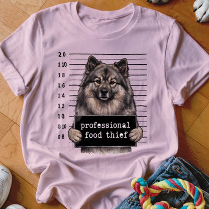 Keeshond dog mugshot with "professional food thief" sign on a pink t-shirt.
