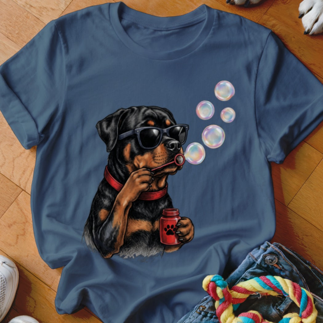 A blue t-shirt printed with a graphic of a Rottweiler wearing sunglasses and blowing soap bubbles.