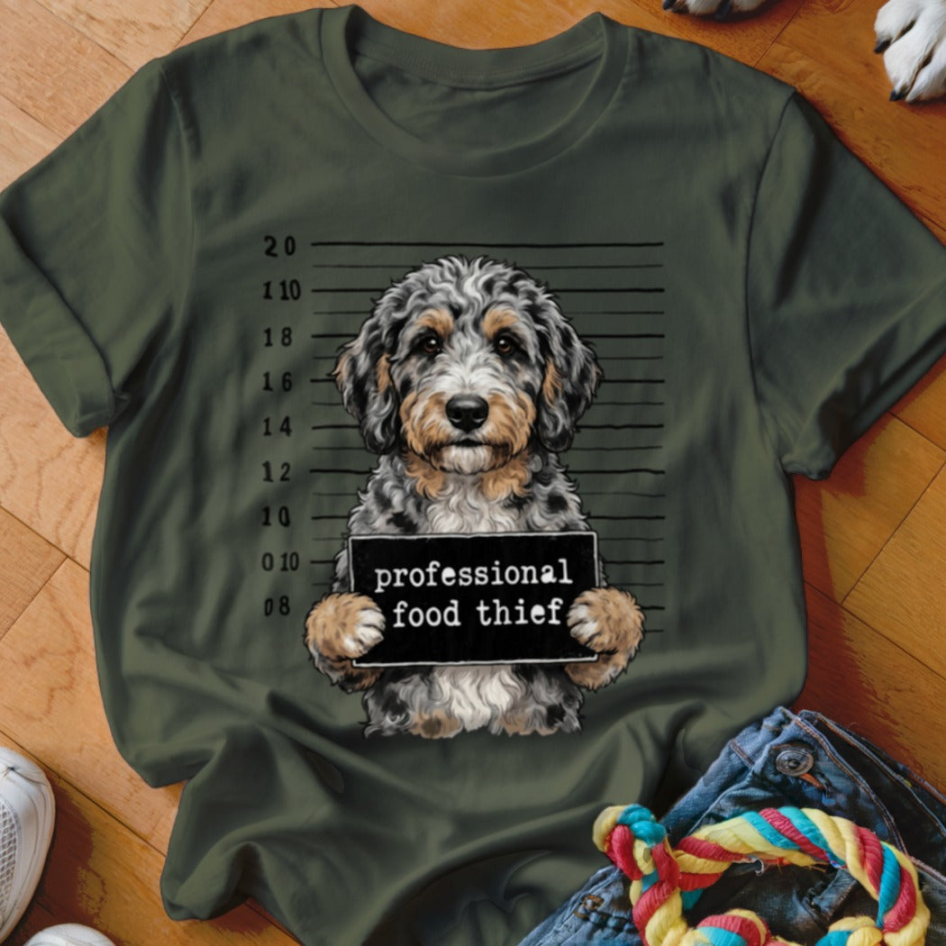 Doodle dog mugshot with "professional food thief" sign on a green t-shirt.