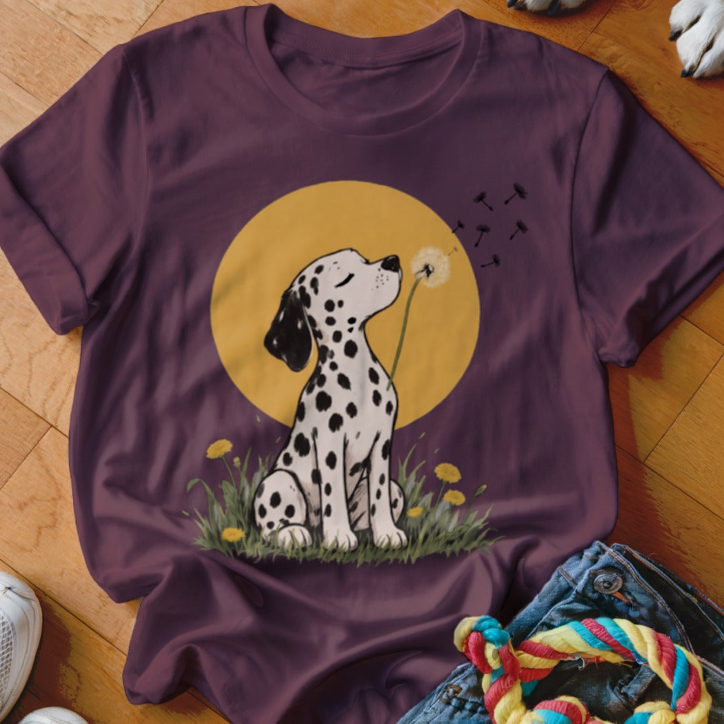 Maroon t-shirt featuring a graphic of a spotted dalmatian puppy blowing dandelion seeds against a yellow moon.