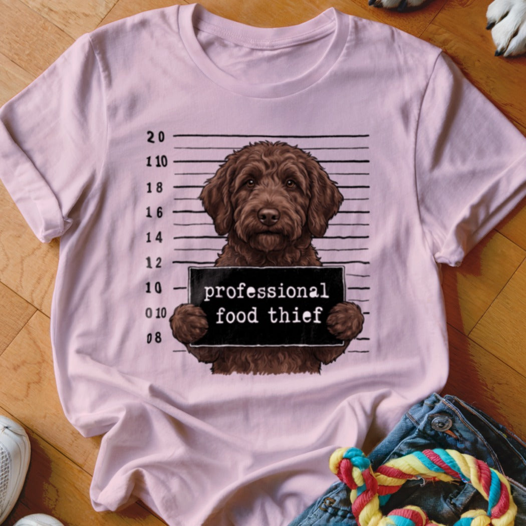 Brown dog mugshot with "professional food thief" sign on a pink t-shirt.