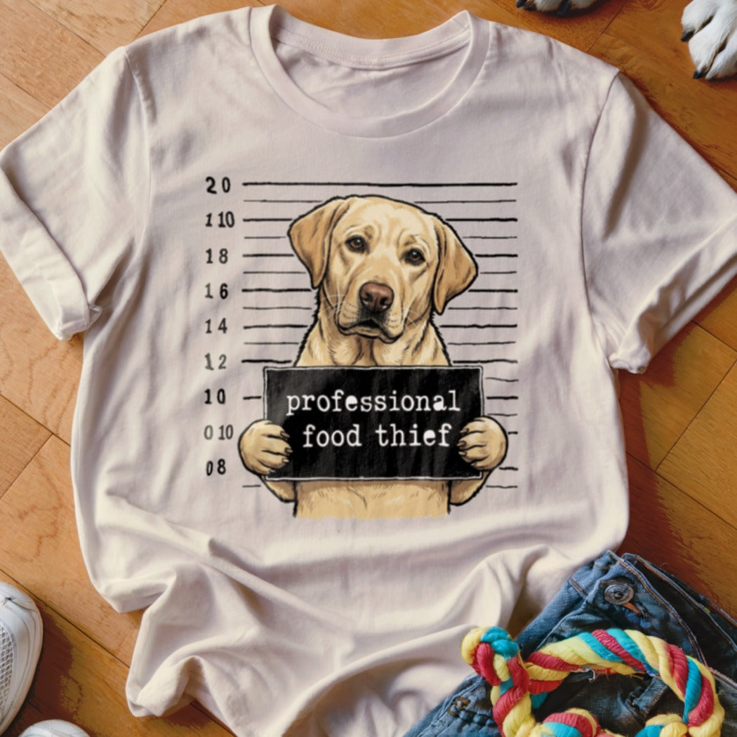 Labrador retriever mugshot with "professional food thief" sign on a t-shirt.