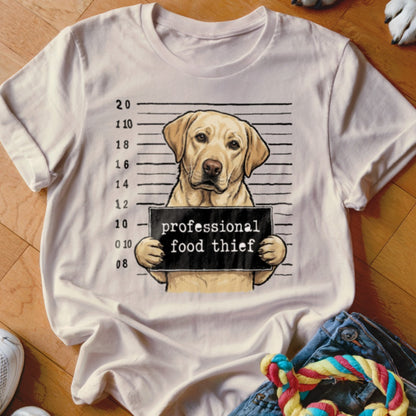 Labrador retriever mugshot with "professional food thief" sign on a t-shirt.