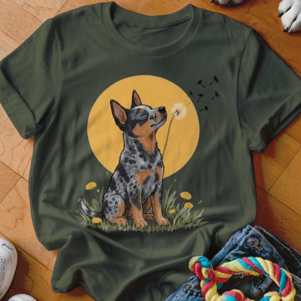 A dark green t-shirt featuring a graphic of an Australian Cattle Dog sitting in a field, blowing dandelion seeds in front of a yellow moon.