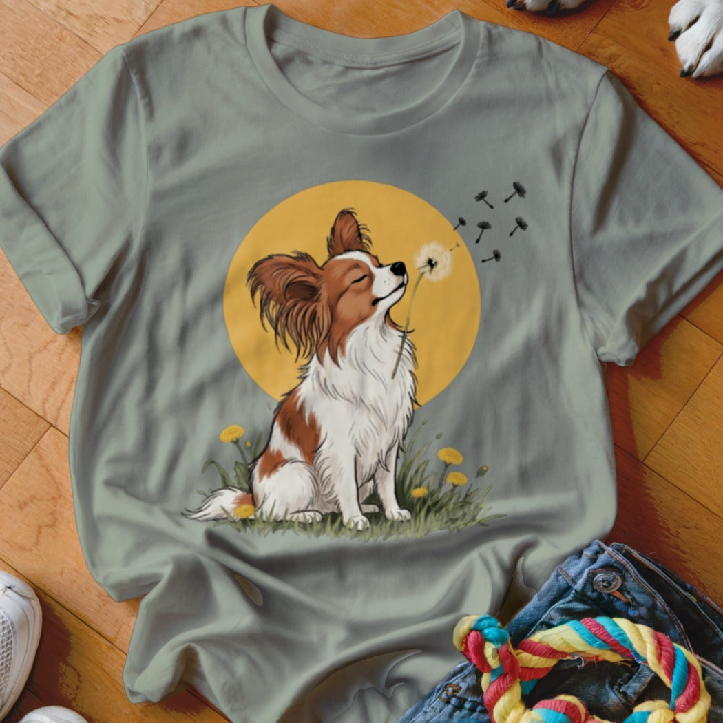 An olive green t-shirt featuring a graphic of a Papillon dog blowing dandelion seeds.