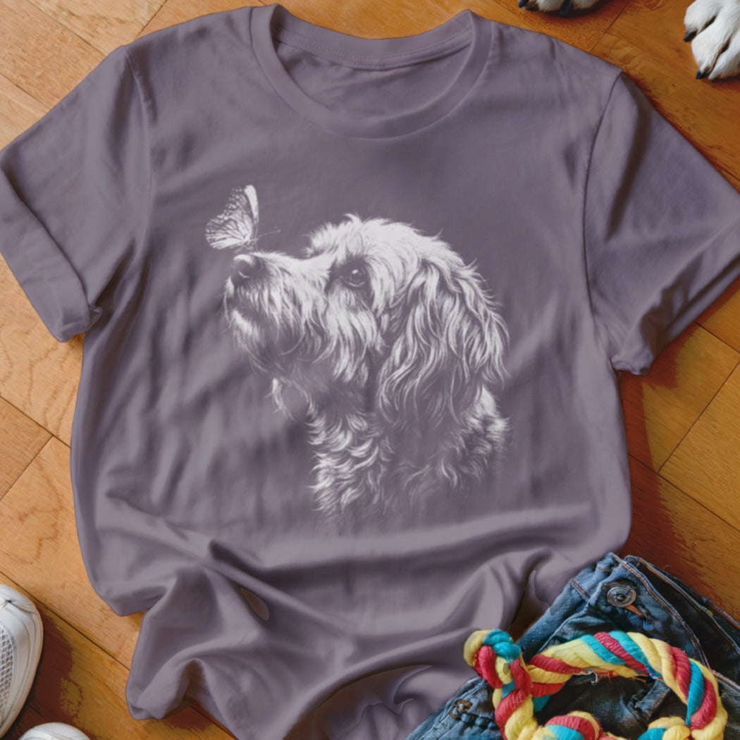 A purple crewneck t-shirt featuring a white line drawing of a fluffy dog and butterfly.