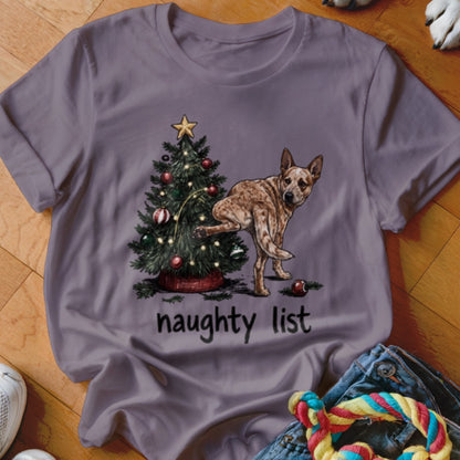Red heeler dog by Christmas tree with text "naughty list" on purple shirt.