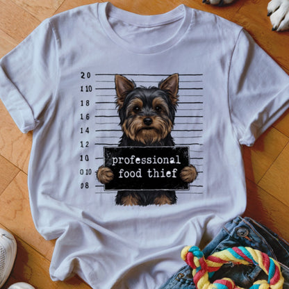Yorkshire Terrier mugshot with "professional food thief" sign on a white t-shirt.